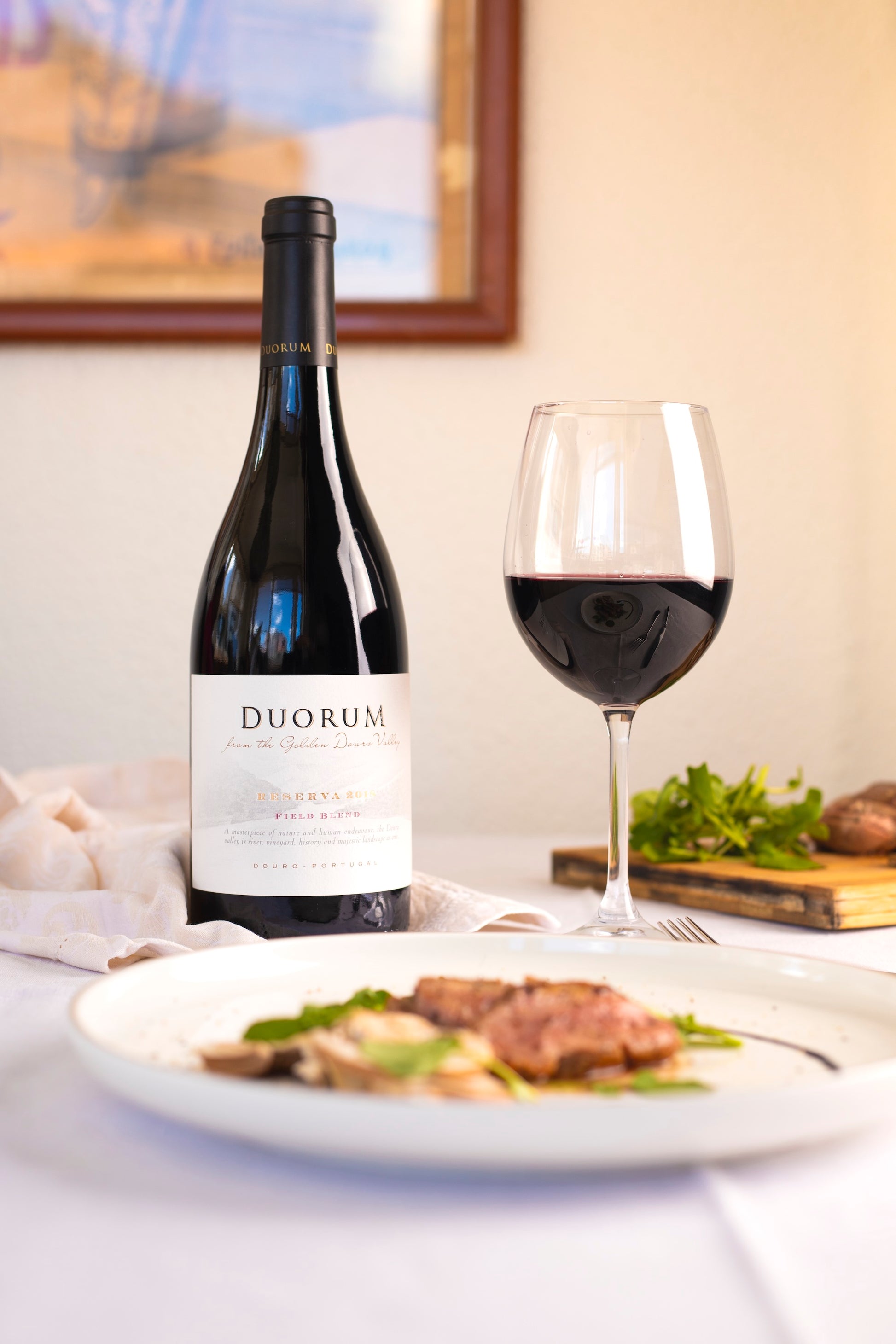 Duorum Reserva Field Blend 2021 red wine elegantly paired with a gourmet meal, featuring a glass of wine and fresh greens.