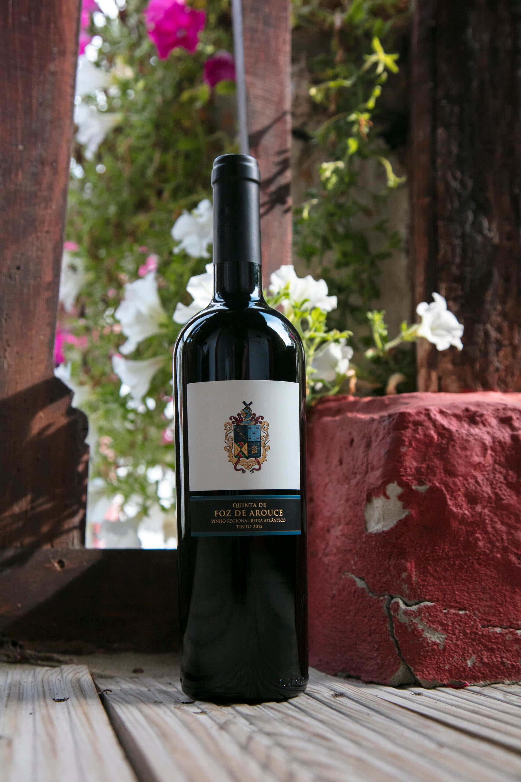 Quinta de Foz de Arouce 2020 red wine elegantly displayed on rustic wooden planks, surrounded by vibrant flowers and natural textures.