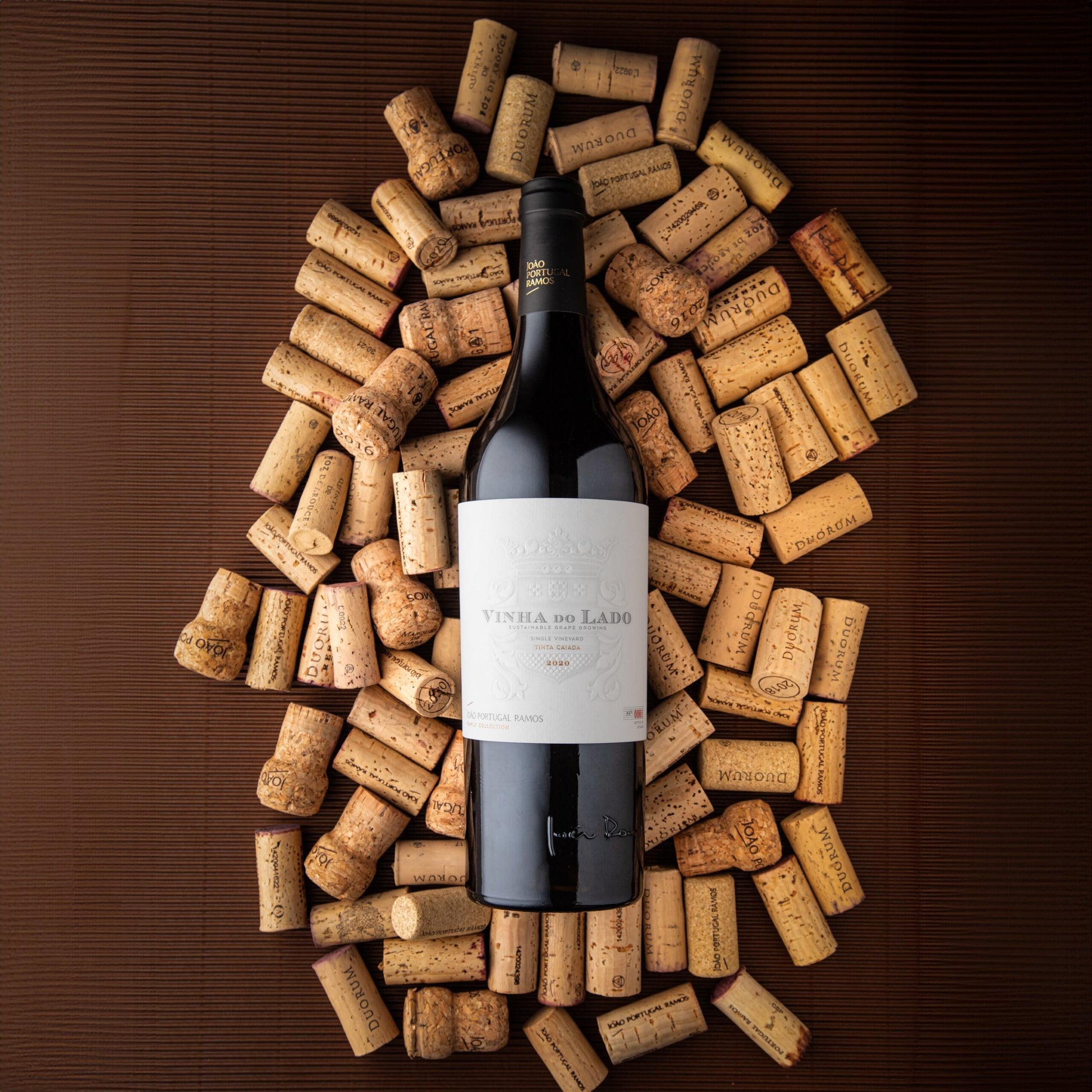 Red Wine: Vinha do Lado (2020) placed on a dark surface, surrounded by numerous corks with various imprints.