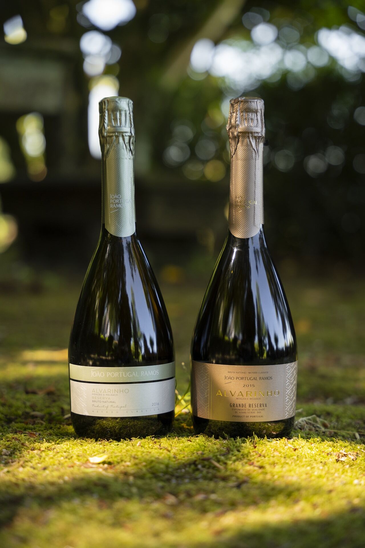 Two bottles from João Portugal Ramos' Alvarinho sparkling wine collection: the 2015 Grande Reserve, available in the shop, next to the 2016 Reserve Brut edition, displayed in a natural setting.